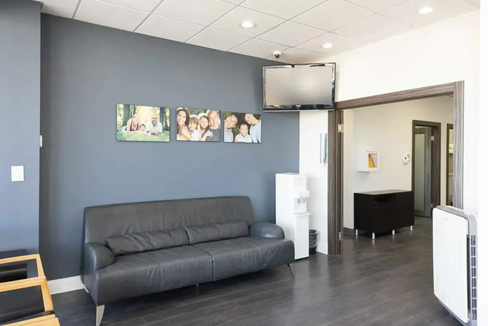 Modern waiting room with gray leather sofa, mounted TV, and family photo canvases.