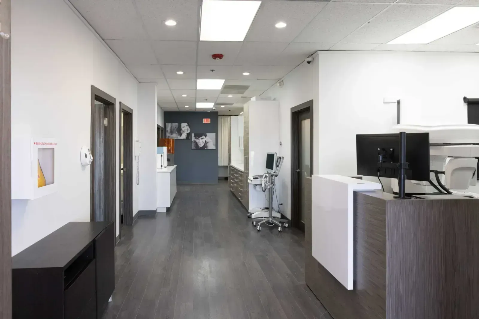 Modern dental office hallway with medical equipment, monitors, and defibrillator cabinet.
