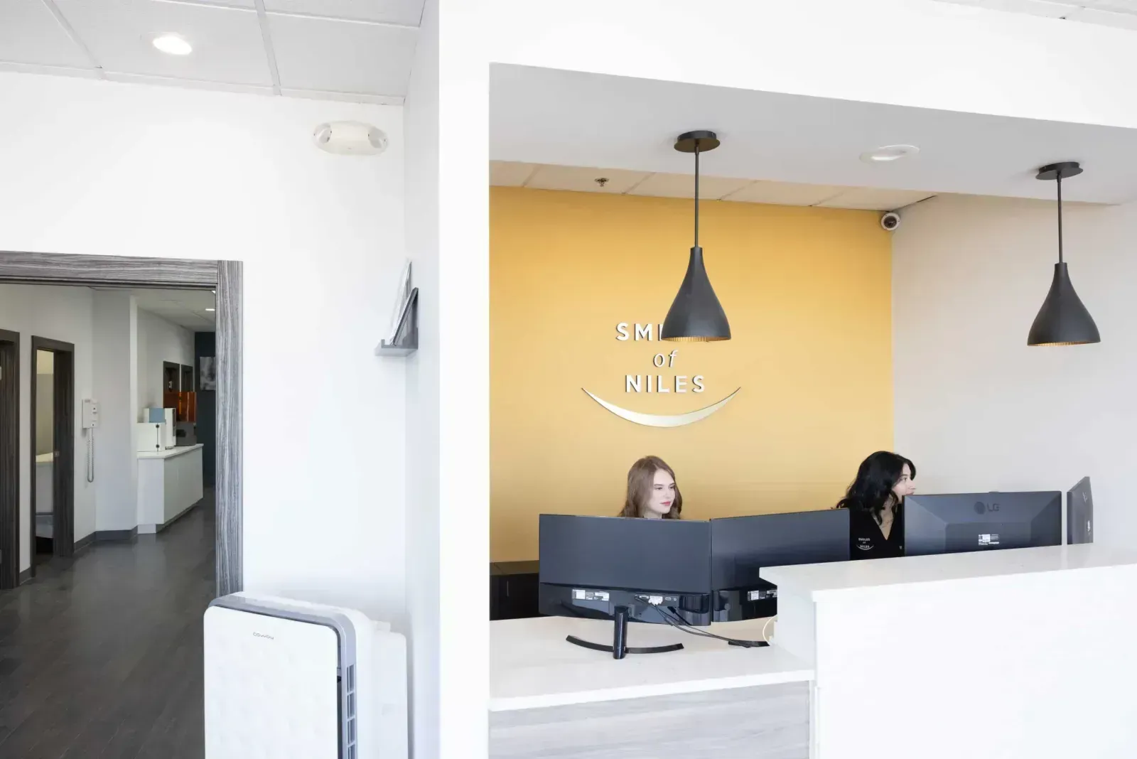 Reception desk at "Smiles of Niles" dental office with two staff members and computer monitors.