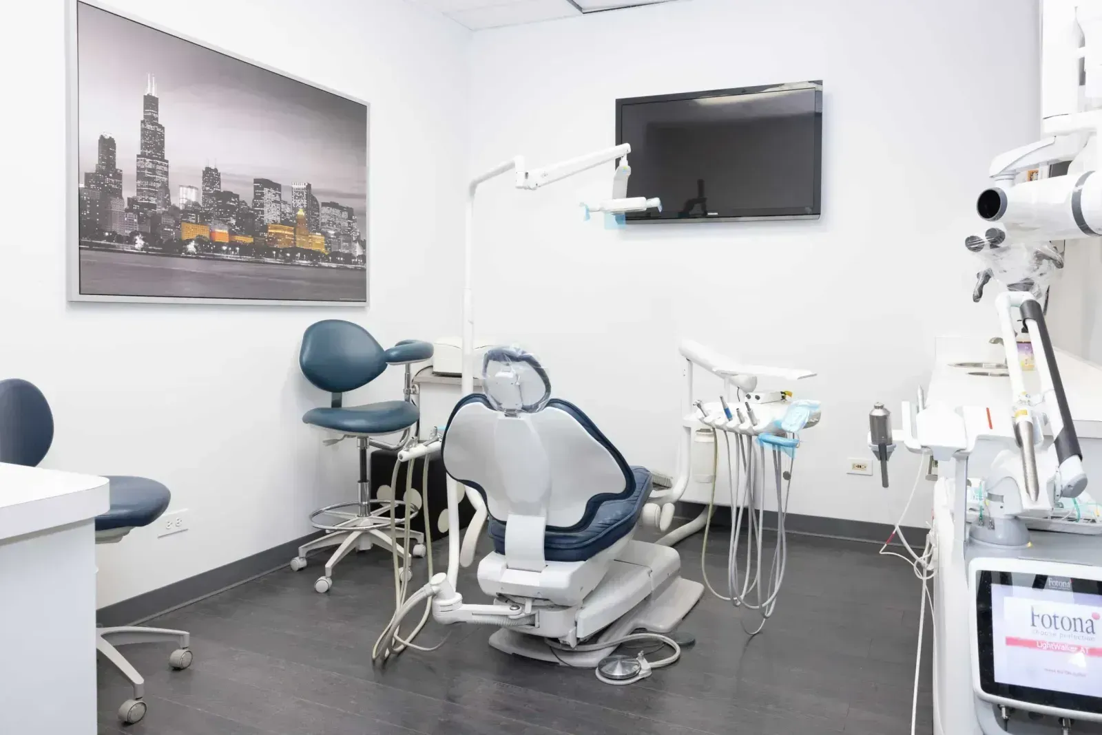 Modern dental treatment room with reclined chair, equipment tray, and Chicago skyline artwork.