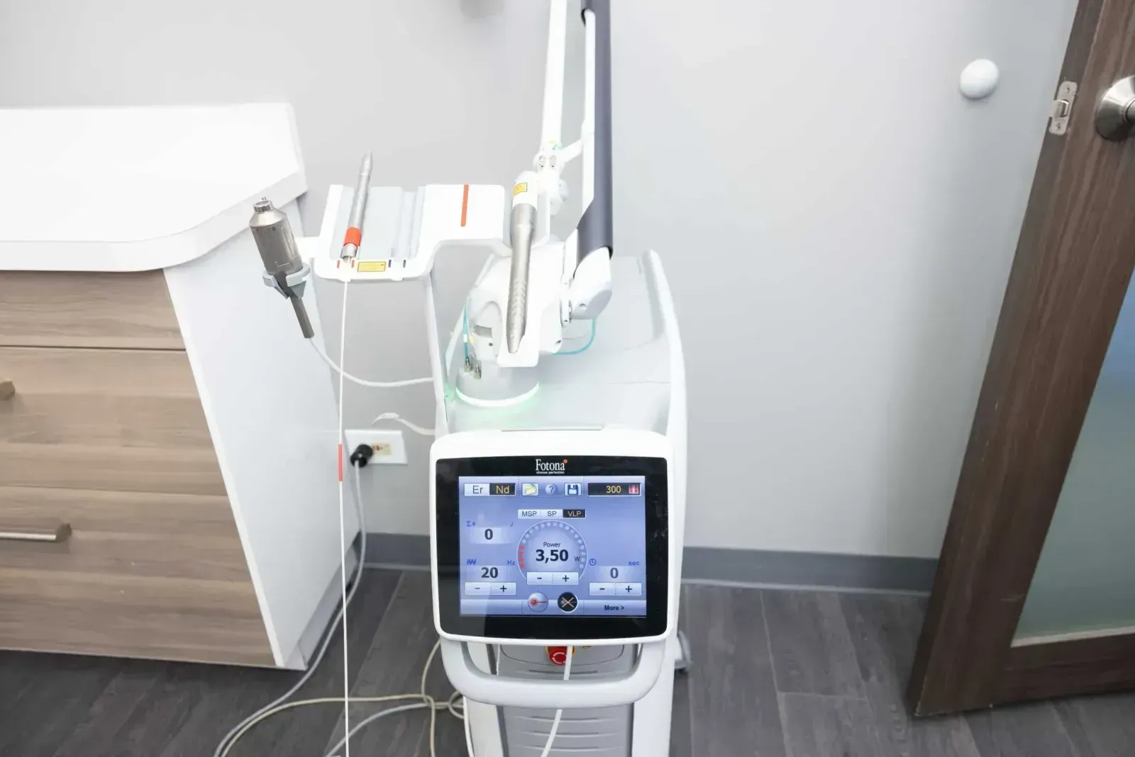 Fotona laser medical device with touchscreen control panel and handpieces in clinic room.