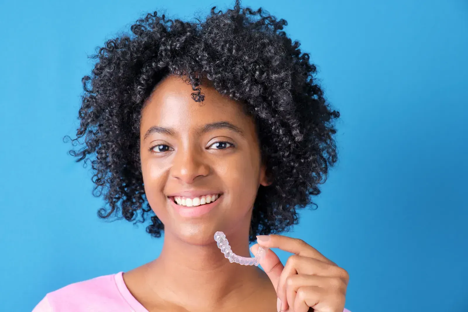 Adult patient smiling while holding a clear Invisalign aligner at Smiles of Niles dental clinic